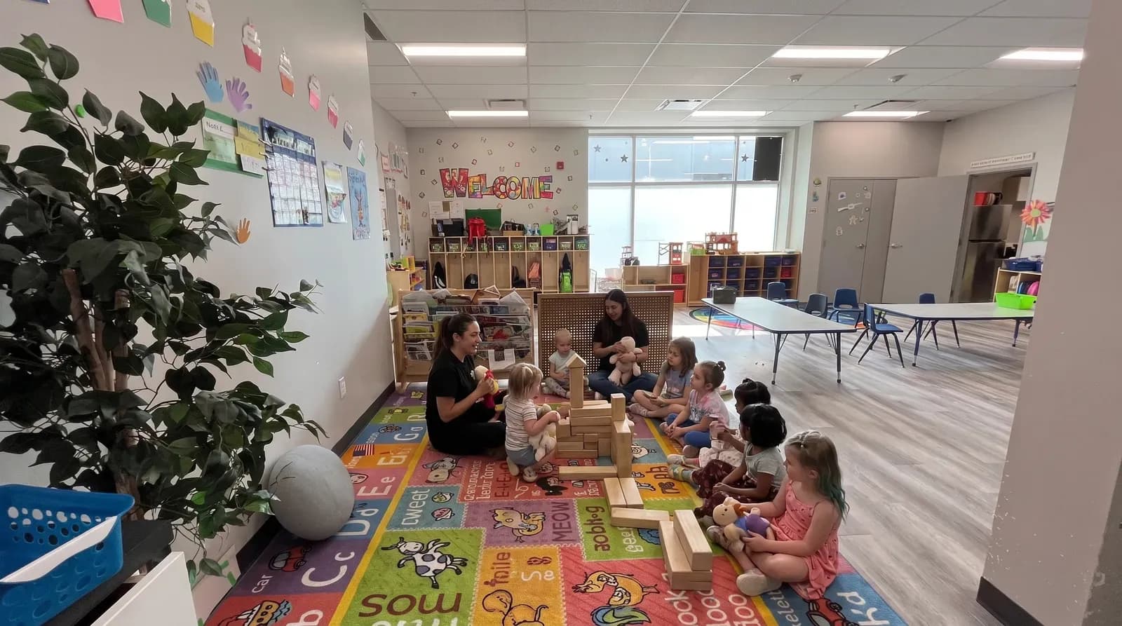 Children building with blocks on an alphabet rug with an educator at Playbox